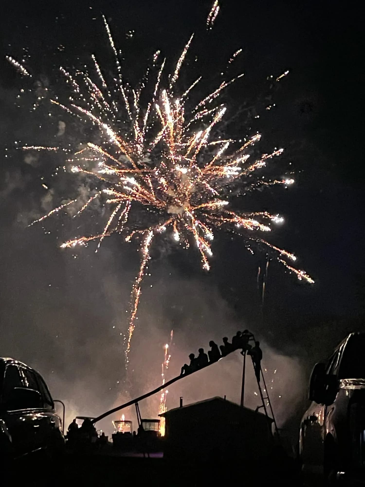 A gold firework bursting above campers watching from below