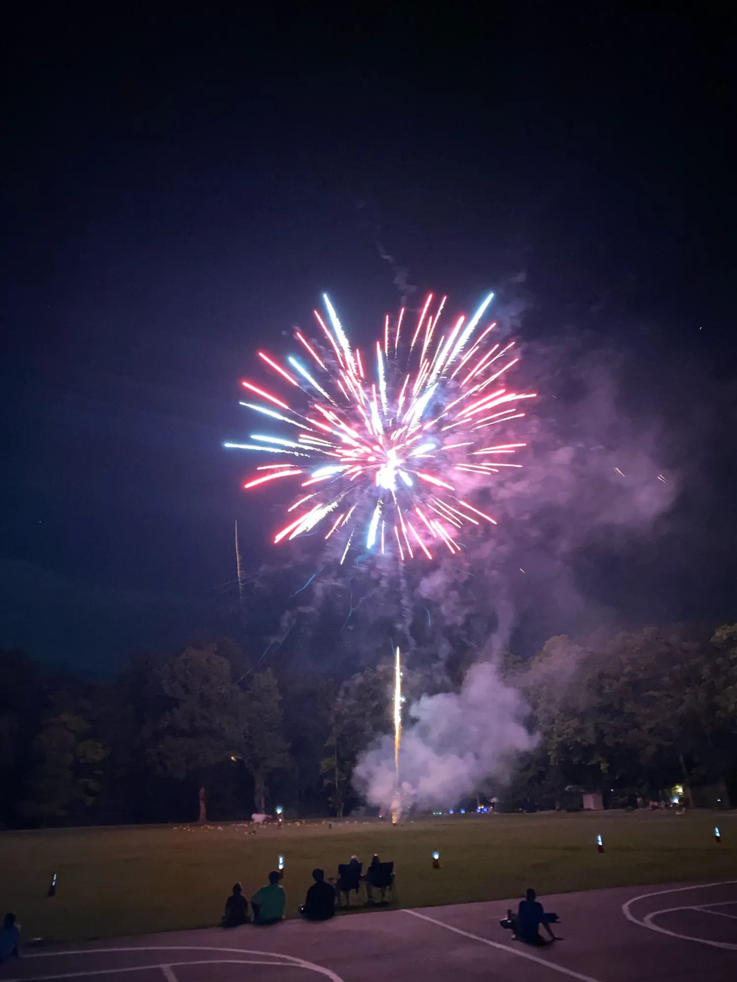 Red, white, and blue fireworks over campers watching from the field