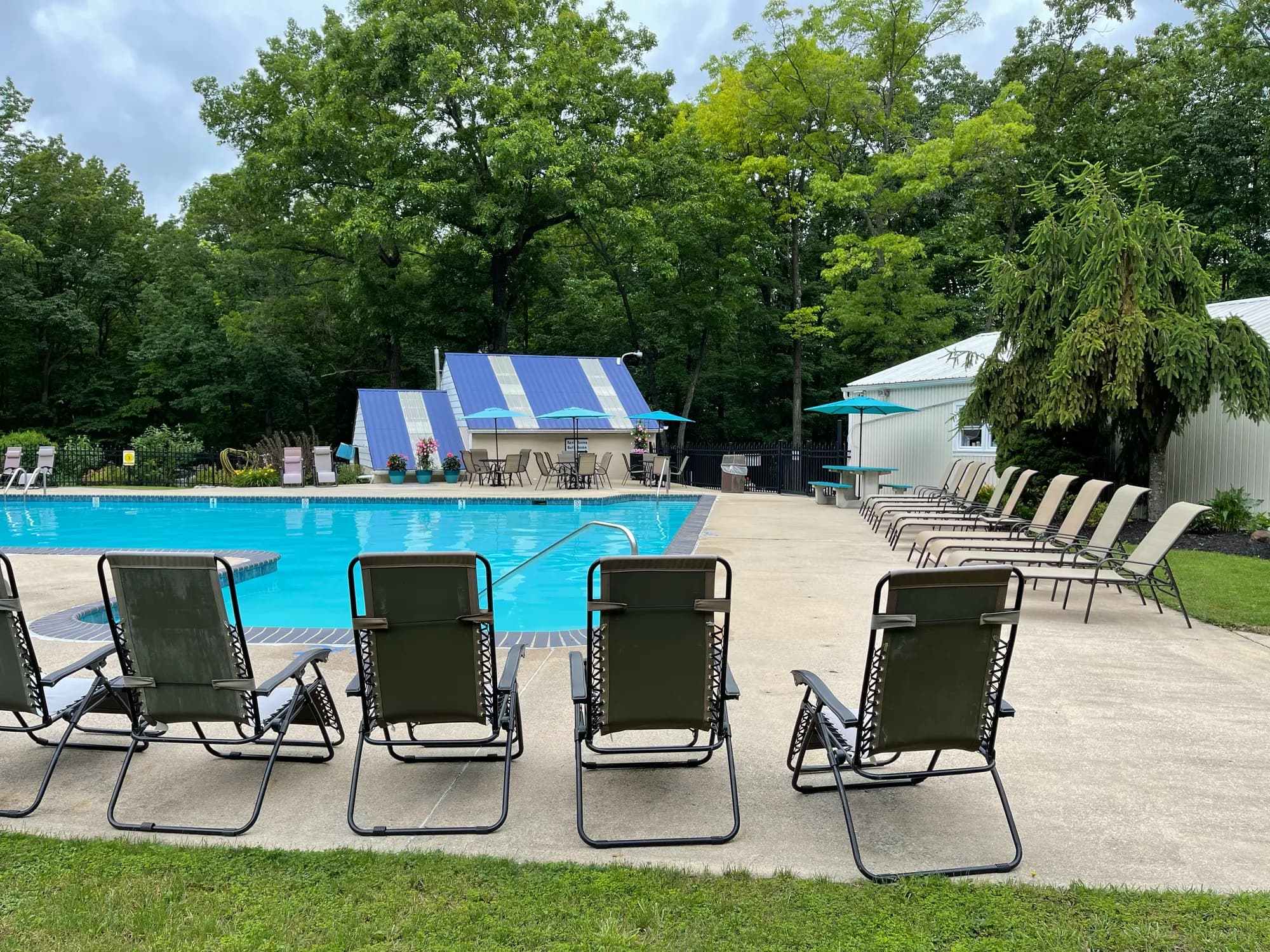 Poolside lounge chairs and a striped shade tent surrounded by trees